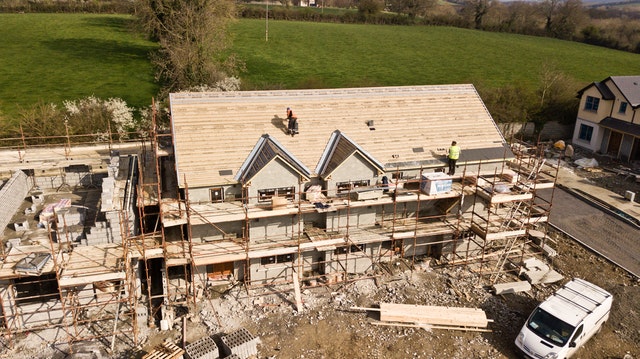An image of a construction site where a new house is beeing build and roofers are working on the roof.